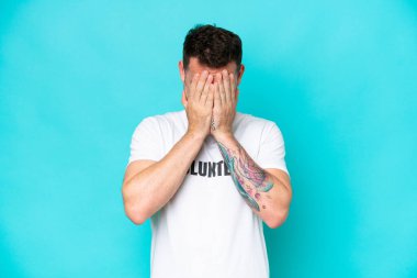 Genç gönüllü beyaz adam mavi arka planda izole edilmiş, yorgun ve hasta bir ifadeyle.