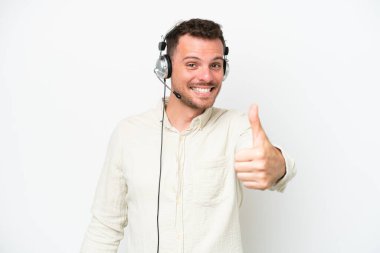 Beyaz arka planda kulaklıkla çalışan beyaz pazarlamacı beyaz bir adam. Başparmakları havada. Çünkü iyi bir şey oldu.