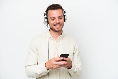Beyaz arka planda izole edilmiş bir kulaklıkla çalışan beyaz pazarlamacı, cep telefonuyla bir mesaj gönderiyor.