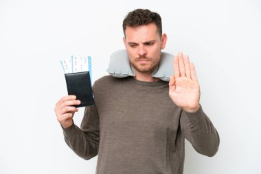 Beyaz arka planda pasaport taşıyan genç beyaz bir adam dur hareketi yapıyor ve hayal kırıklığına uğruyor.