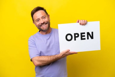 Sarı arka planda izole edilmiş orta yaşlı beyaz bir adam elinde mutlu bir ifadeyle barış sembolü taşıyan bir pankart tutuyor.