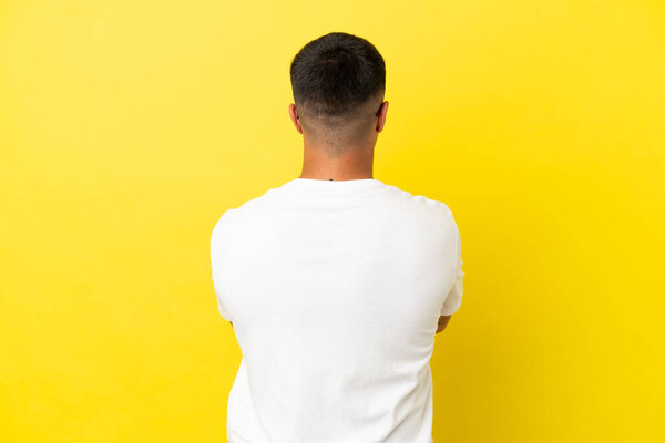 Young handsome man over isolated yellow background in back position