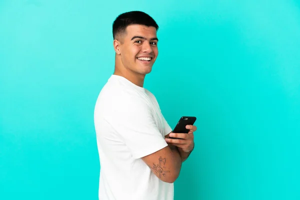 Молодий Красивий Чоловік Над Ізольованим Синім Тлом Тримає Мобільний Телефон — стокове фото