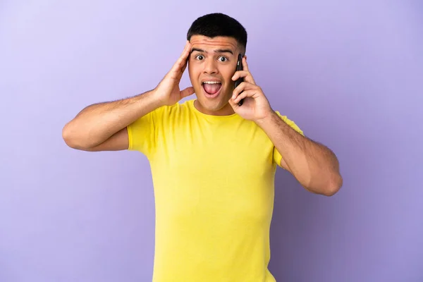 Молодой Красивый Мужчина Использует Мобильный Телефон Изолированном Фиолетовом Фоне Удивлением — стоковое фото