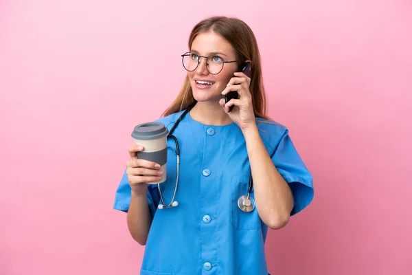 一位年轻的外科医生女医生被隔离在粉红的背景下 手里拿着咖啡和手机 — 图库照片