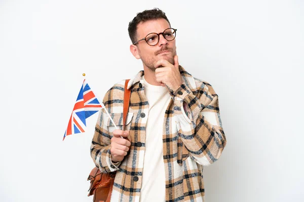 年轻的恐慌性男子举着一面英国国旗 背景为白色 有着怀疑和思考 — 图库照片