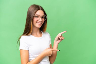 İzole edilmiş arka planda genç beyaz bir kız parmak göstererek bir ürün sunuyor.