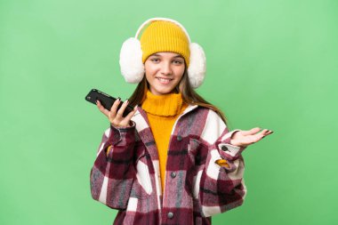 Kafkasyalı genç bir kız izole edilmiş arka planda kışlık kuklalar takıyor cep telefonuyla sohbet ediyor.