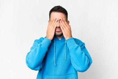 İzole edilmiş beyaz arka planda genç, yakışıklı beyaz bir adam. Gözlerini elleriyle kapatıyor.