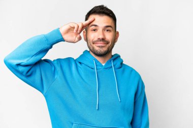 Young handsome caucasian man over isolated white background saluting with hand with happy expression