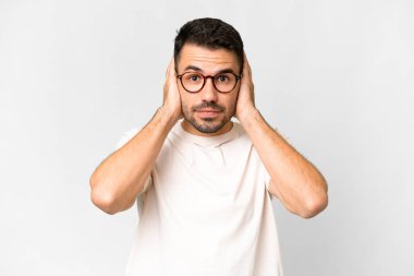 İzole edilmiş beyaz arka planı olan yakışıklı beyaz adam hayal kırıklığına uğramış ve kulaklarını kapatmış.