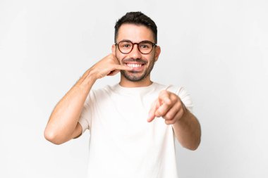 Beyaz arka planda yaşayan yakışıklı beyaz bir adam telefon jesti yapıyor ve ön tarafı işaret ediyor.