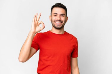 İzole edilmiş beyaz arka plan üzerinde yakışıklı beyaz bir adam parmaklarıyla tamam işareti gösteriyor.