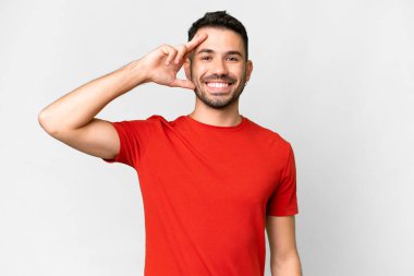 Young handsome caucasian man over isolated white background saluting with hand with happy expression