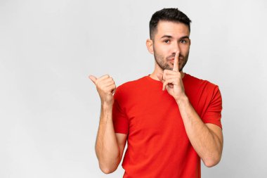 İzole edilmiş beyaz arka planda genç, yakışıklı beyaz bir adam. Yan tarafı işaret ediyor ve sessiz hareketler yapıyor.