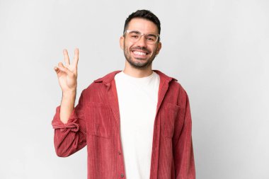 Beyaz arka planda yaşayan yakışıklı beyaz adam gülümsüyor ve zafer işareti gösteriyor.