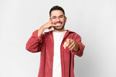 Beyaz arka planda yaşayan yakışıklı beyaz bir adam telefon jesti yapıyor ve ön tarafı işaret ediyor.