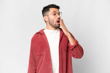 İzole edilmiş beyaz arka planda genç, yakışıklı beyaz bir adam esniyor ve ağzını eliyle kapatıyor.