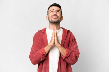 Young handsome caucasian man over isolated white background keeps palm together. Person asks for something