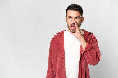 Young handsome caucasian man over isolated white background whispering something with surprise gesture while looking to the side