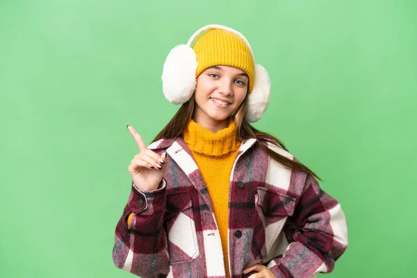 年轻的高加索女孩披着冬衣 站在与世隔绝的背景上 展示并举起一个手指 表示她是最好的 — 图库照片