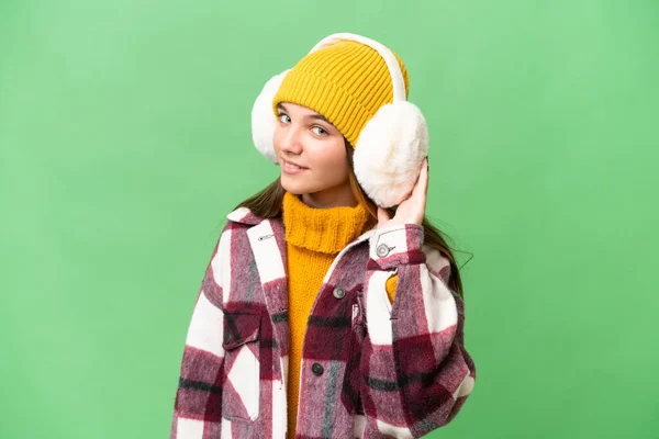 十几岁的白人女孩披着冬衣 在与世隔绝的背景下听着什么 用手捂住耳朵 — 图库照片