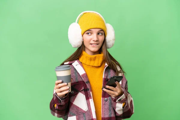 ティーンCaucasian女の子身に着けています冬ムフ上の隔離された背景保持コーヒーへ取り去ると携帯何かを考えながら — ストック写真