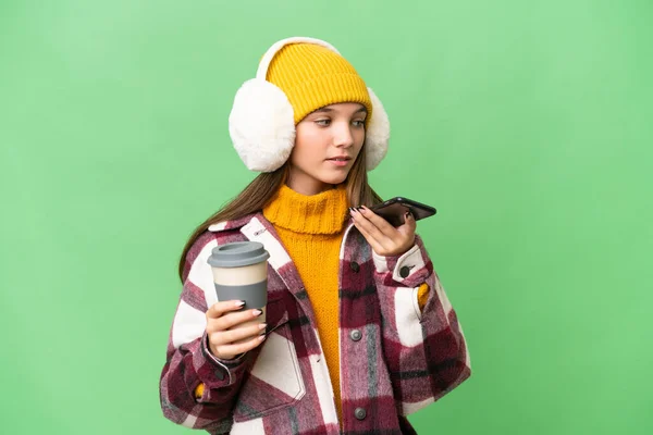 年轻的高加索女孩穿着冬衣 背景偏僻 手里拿着咖啡和手机 — 图库照片