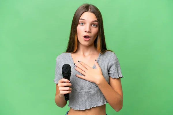 stock image Teenager singer girl picking up a microphone over isolated background surprised and shocked while looking right