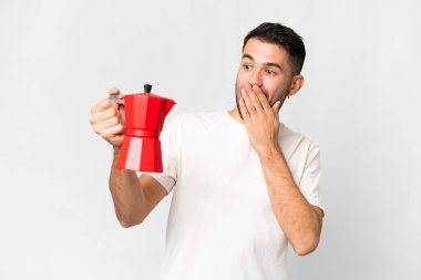 Young caucasian man holding coffee pot over isolated white background with surprise and shocked facial expression