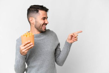 İzole edilmiş beyaz arka planda kızarmış cipsleri tutan genç beyaz bir adam parmak gösterip bir ürün sunuyor.