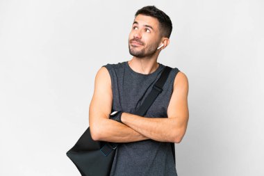 İzole edilmiş beyaz arka planda spor çantasıyla genç beyaz adam omuzlarını kaldırırken şüpheyle hareket ediyor.
