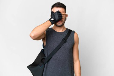 İzole edilmiş beyaz arka plan üzerinde spor çantalı beyaz tenli genç bir beyaz adam elleriyle gözlerini kapatıyor. Bir şey görmek istemiyorum.