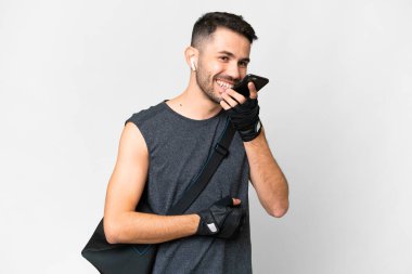 İzole edilmiş beyaz arka planda spor çantalı beyaz bir genç adam cep telefonuyla sohbet ediyor.