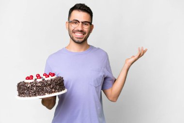 Young caucasian man holding birthday cake isolated on white background extending hands to the side for inviting to come