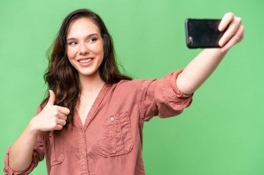 Kafkasyalı genç bir kadın izole edilmiş arka planda cep telefonuyla selfie çekiyor.