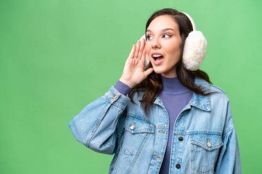 İzole edilmiş arka planda kışlık manşet takan beyaz bir kadın kulağına elini sürerek bir şeyler dinliyor.