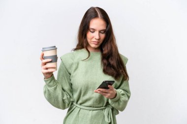 Beyaz arka planda izole edilmiş genç beyaz bir kadın kahve alıp götürmek için elinde bir cep telefonu...