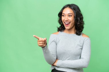 Arjantinli genç bir kadın izole edilmiş arka planda parmağını kenarı gösteriyor ve bir ürün sunuyor.