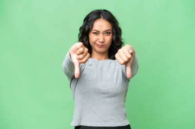 Arjantinli genç bir kadın izole edilmiş arka planda baş parmağını iki eliyle gösteriyor.