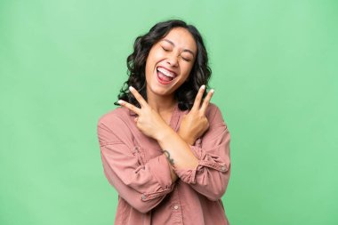 Arjantinli genç bir kadın izole edilmiş arka planda gülümsüyor ve zafer işareti gösteriyor.