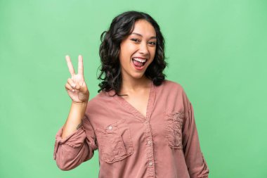 Arjantinli genç bir kadın izole edilmiş arka planda gülümsüyor ve zafer işareti gösteriyor.