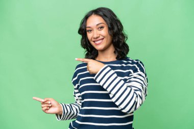 Arjantinli genç bir kadın izole edilmiş arka planda parmağını kenarı gösteriyor ve bir ürün sunuyor.