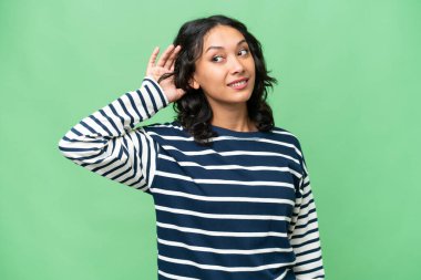 Arjantinli genç bir kadın izole edilmiş arka planda bir şeyler dinlerken elini kulağına koyar.