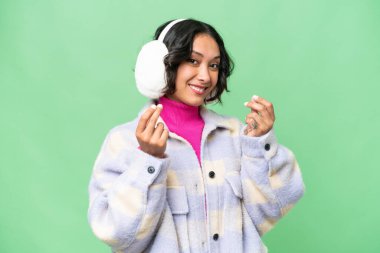 Arjantinli genç bir kadın izole edilmiş arka planda kışlık manşetler takıyor ve para hareketi yapıyor.