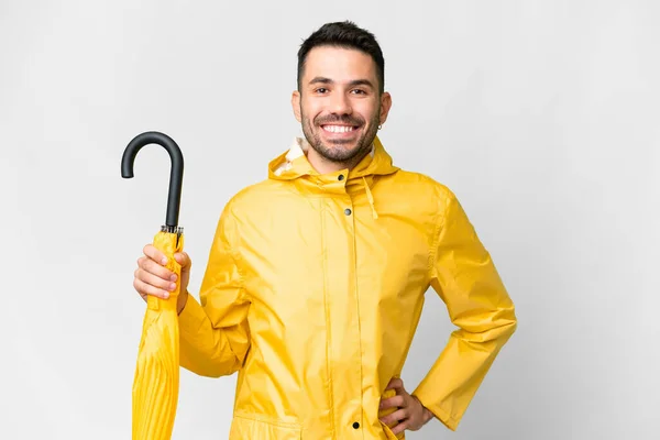 年轻的高加索人 身穿防雨外套 带着雨伞 披着孤零零的白色背景 双手叉腰 面带微笑 — 图库照片