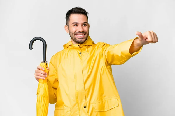 年轻的高加索人 身穿防雨外套 带着雨伞 披着孤零零的白色背景 竖起大拇指做着手势 — 图库照片