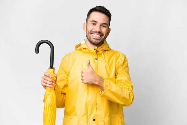 年轻的高加索人 身穿防雨外套 带着雨伞 披着孤零零的白色背景 竖起大拇指做着手势 — 图库照片