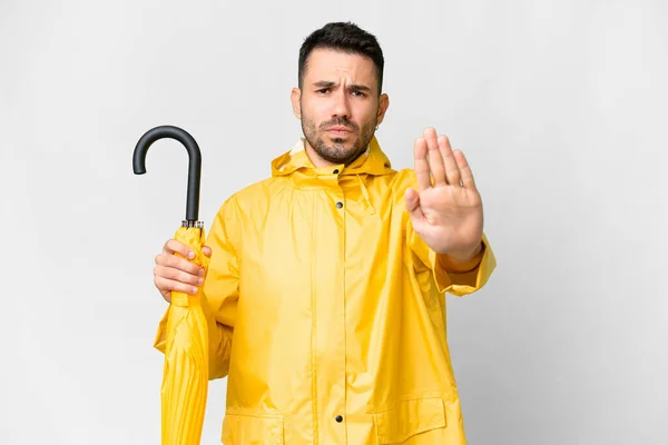 年轻的高加索人 身穿防雨外套 带着雨伞 站在与世隔绝的白色背景之上 做着停止姿势 — 图库照片