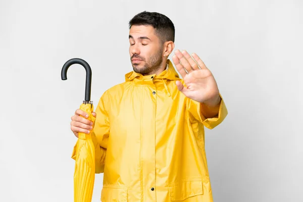 年轻的高加索人 身穿防雨外套 披着雨伞 站在与世隔绝的白色背景之上 做出了停止的姿态 感到失望 — 图库照片